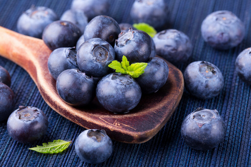 Close-up of fresh blueberries on rustic wooden spoon with green leaves textured dark background Wallpaper