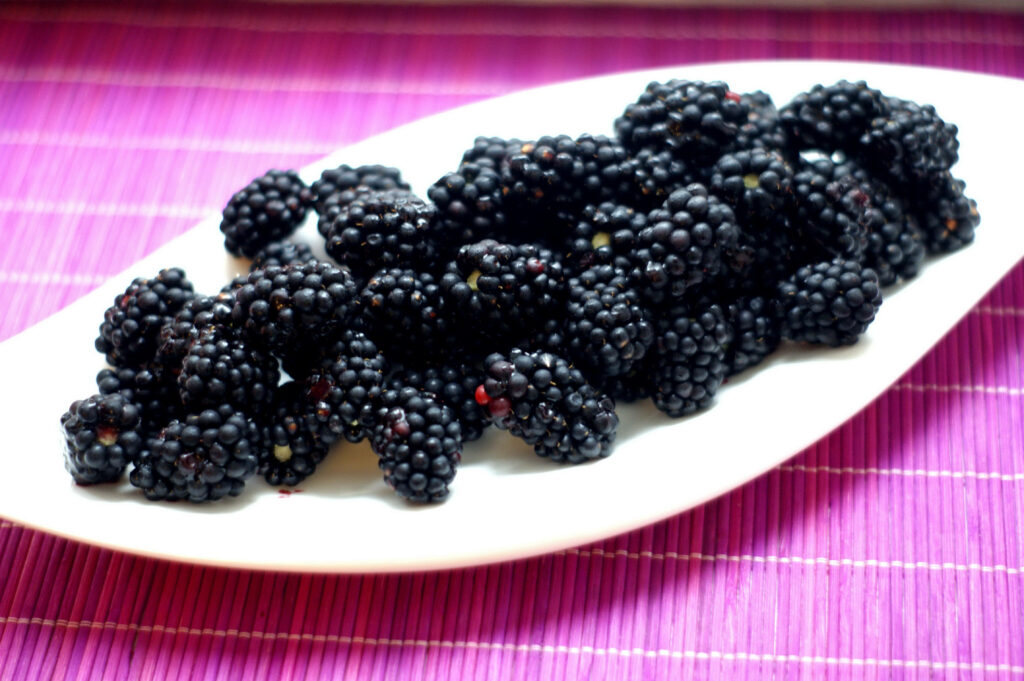 Glossy ripe black mulberries piled on white plate with vibrant purple background wallpaper
