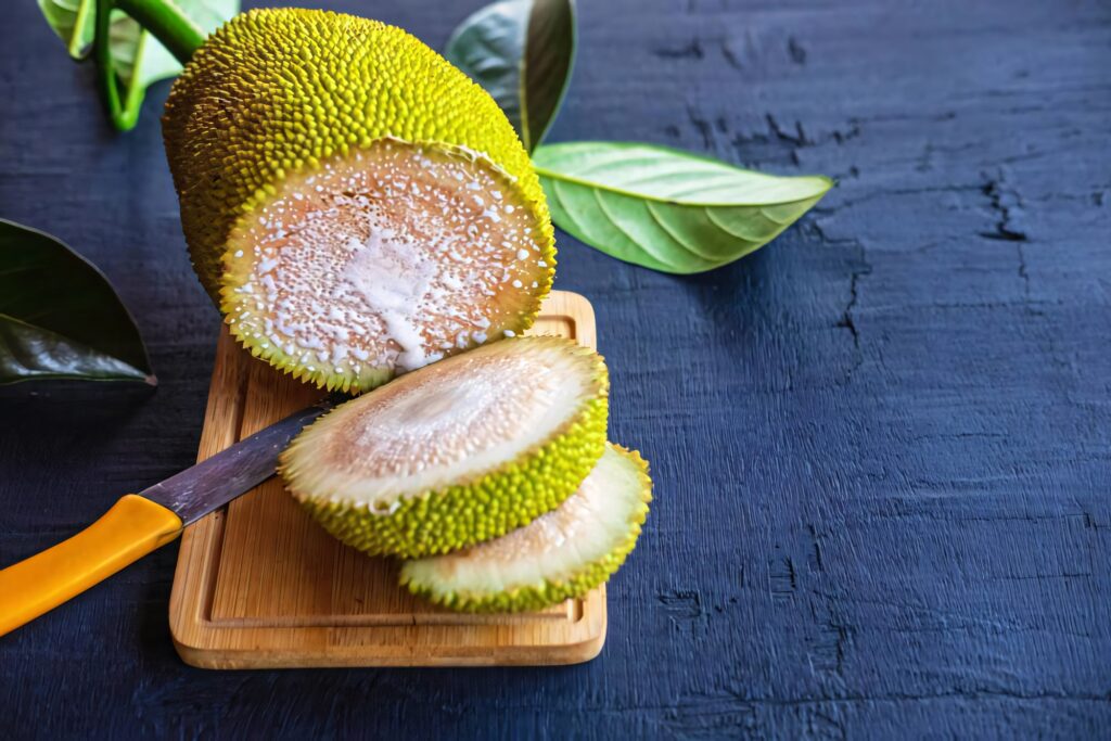 Fresh green breadfruit sliced on wooden board showing fibrous texture with tropical leaves Wallpaper