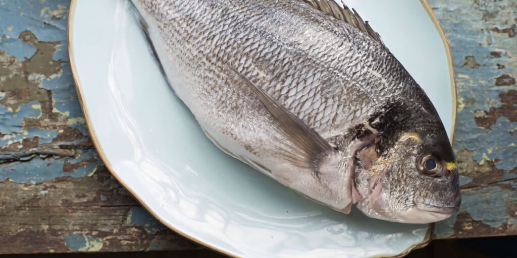 Close-up of fresh silver bream fish on white ceramic plate showcasing natural textures and details Wallpaper