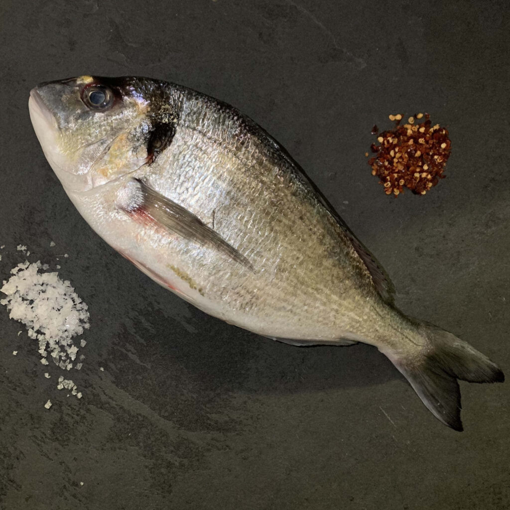 Whole raw bream fish on dark stone with coarse sea salt and cracked black pepper rustic food background Wallpaper