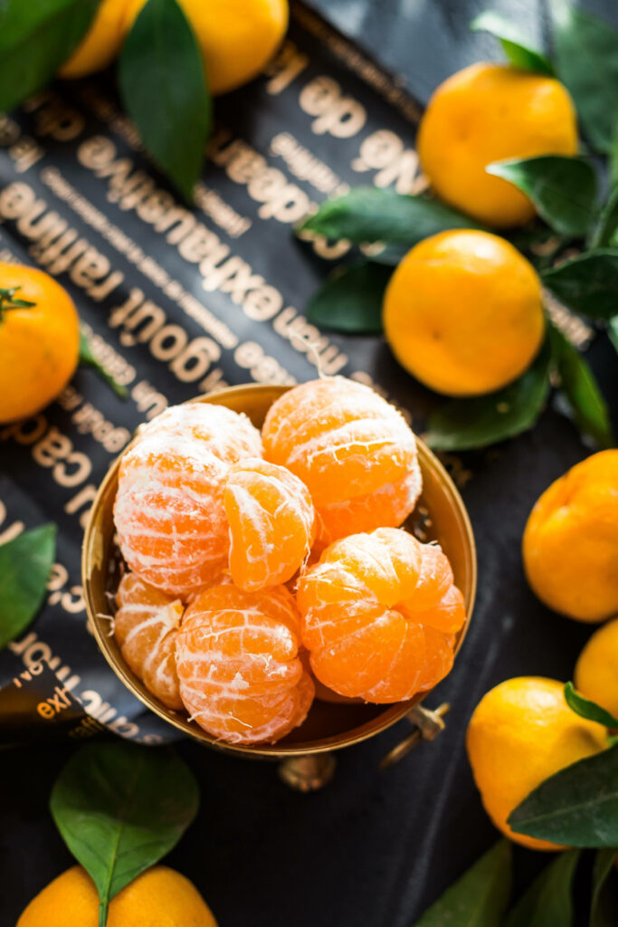 Overhead view of peeled clementine segments with whole citrus fruits and green leaves wallpaper