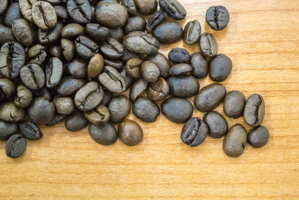 Close-up of fresh glossy coffee beans on smooth wooden surface warm inviting coffee background Wallpaper