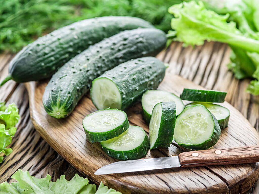 Fresh sliced cucumbers on rustic wooden board with crisp lettuce and vibrant green tones wallpaper