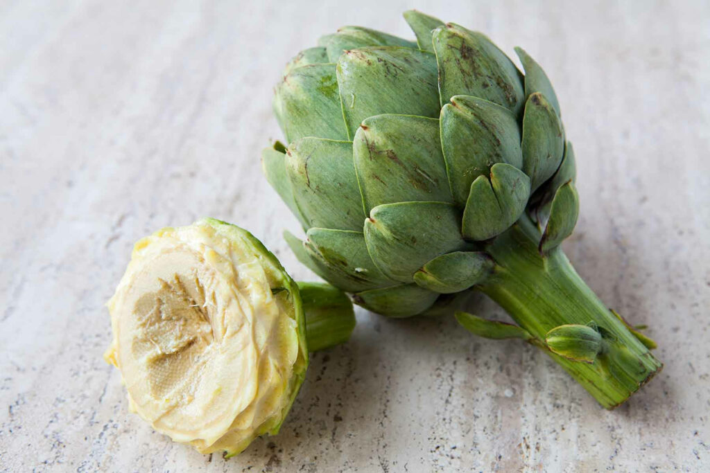 Fresh cut green artichoke showing natural layers on light textured surface wallpaper background