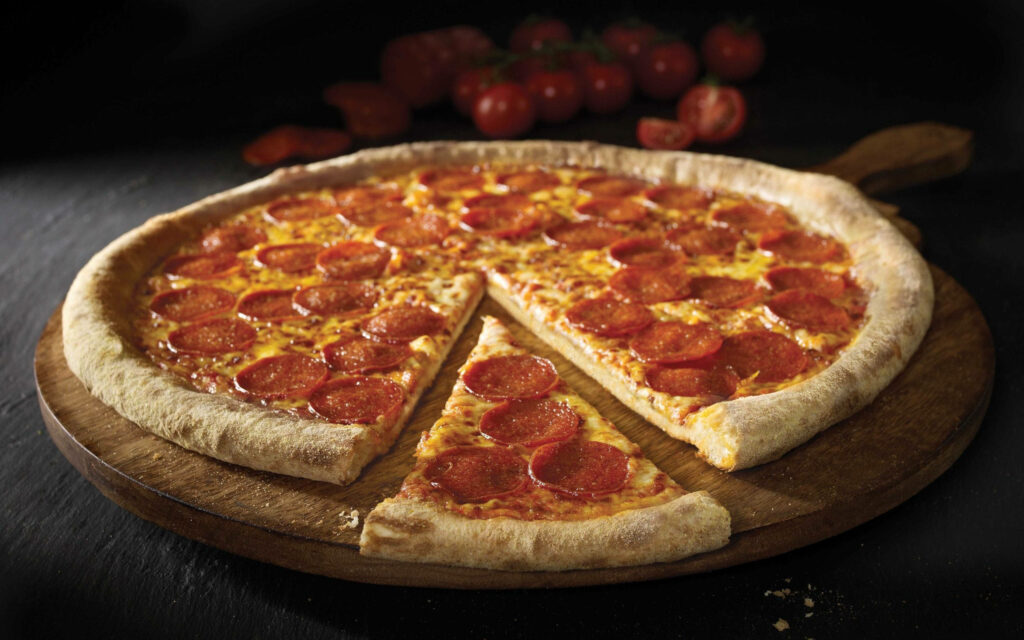 Freshly baked Domino's pepperoni pizza on wooden board with golden crust and ripe tomatoes background Wallpaper