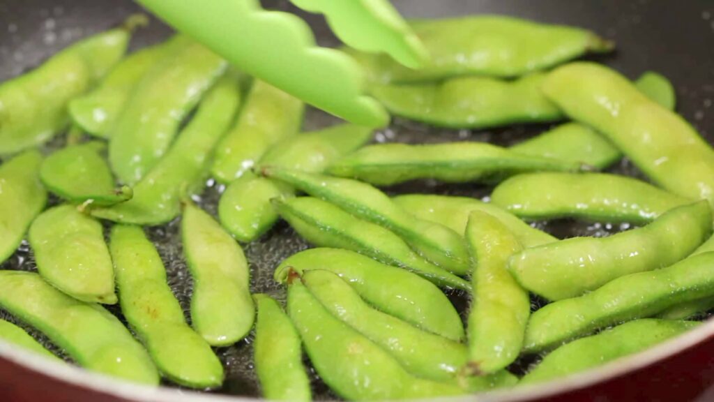 Fresh green edamame beans boiling in a pan with green tongs ready for a healthy snack Wallpaper