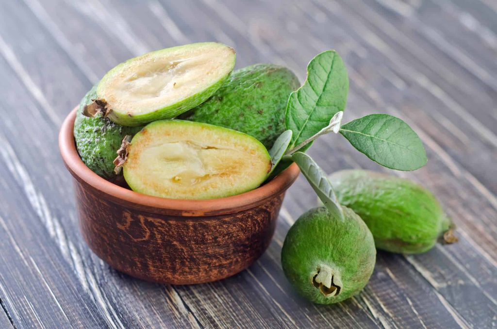 Fresh feijoa fruits whole and halved in clay bowl on rustic wooden table natural light background Wallpaper