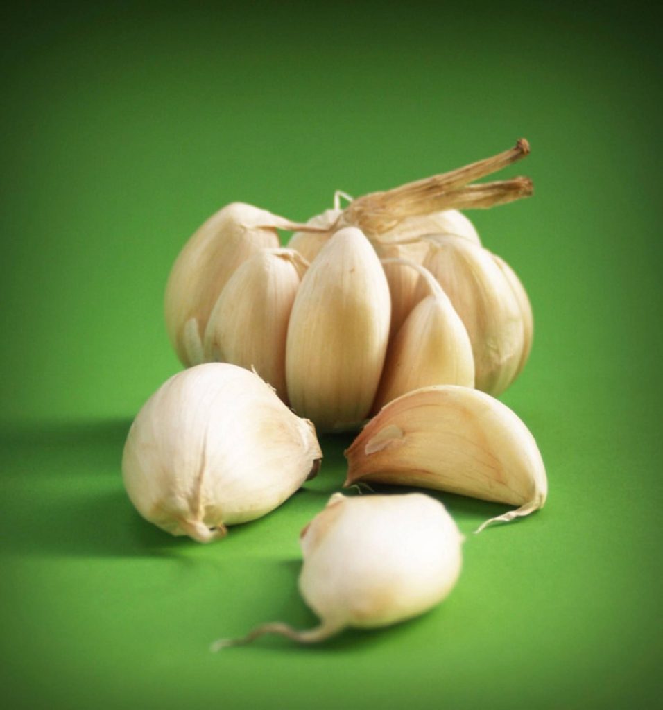 Fresh garlic bulbs and cloves on vibrant green background with soft lighting and organic texture Wallpaper