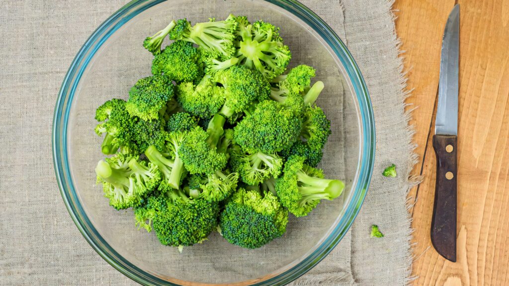 Fresh green broccoli florets in glass bowl on wooden table with knife rustic healthy food background Wallpaper