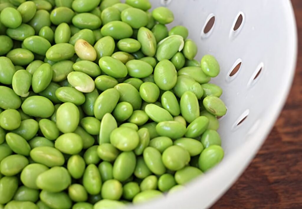 Fresh shelled edamame beans in white colander vibrant green healthy food rustic wooden background Wallpaper