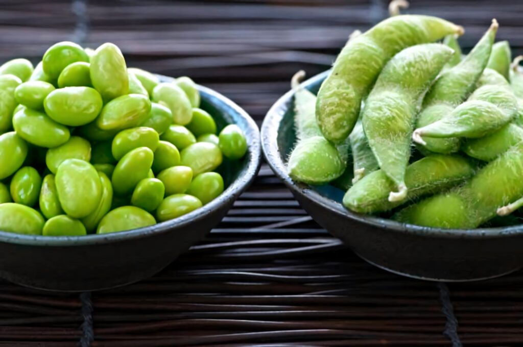 Vibrant green edamame pods and beans in dark bowls on bamboo mat fresh Japanese appetizer wallpaper