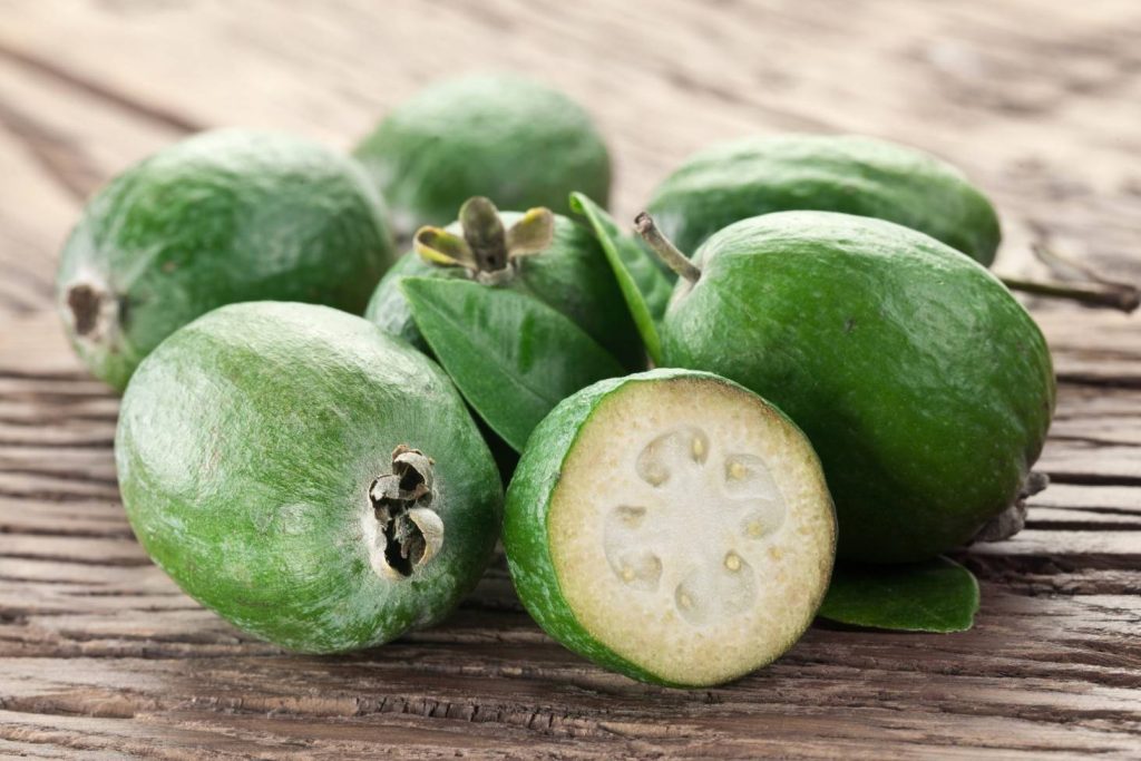 Fresh green feijoas with creamy slices on rustic wooden table natural food wallpaper background