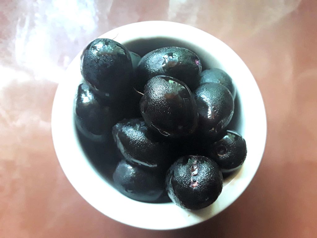 Close-up of fresh glistening Java plums in white bowl on warm wooden table vibrant wallpaper