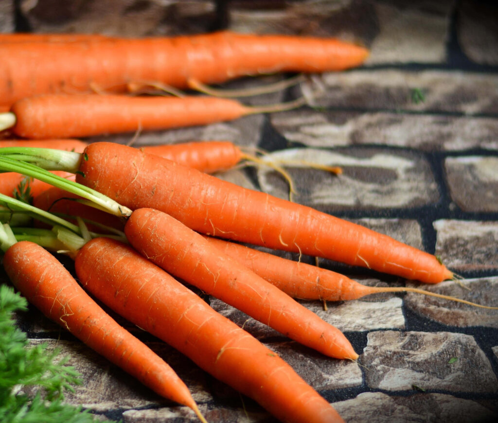 Fresh vibrant orange carrots with green tops on rustic stone surface emphasizing health and nutrition Wallpaper