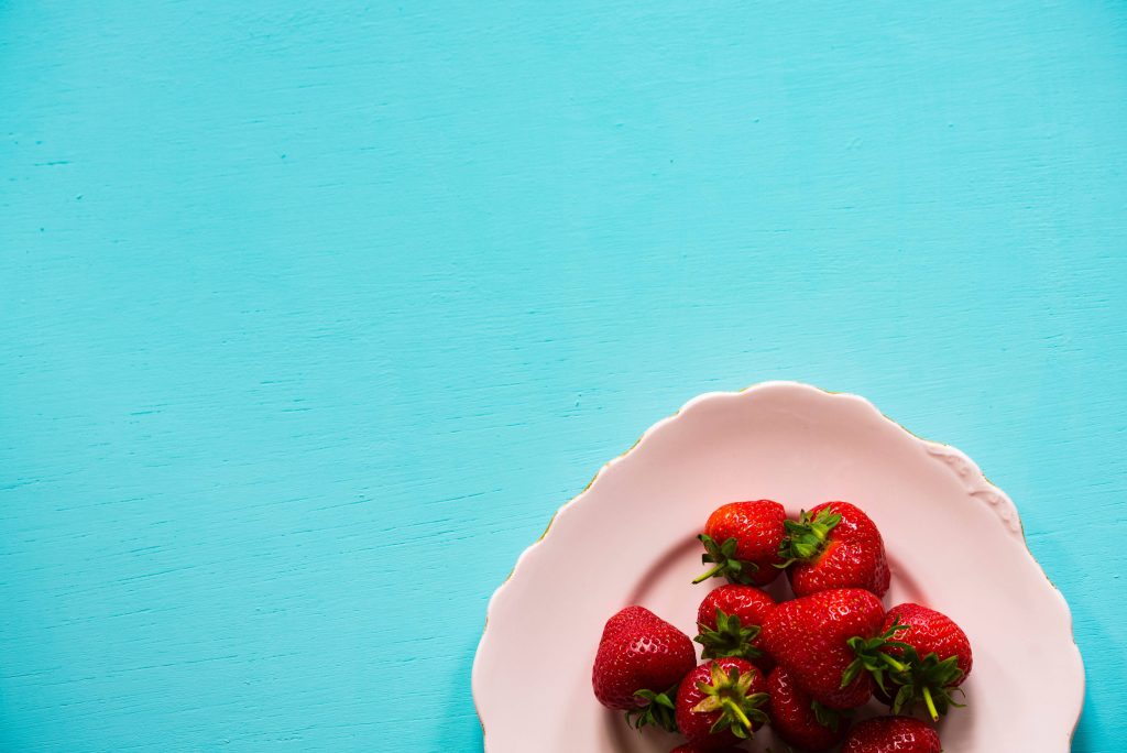 Fresh red strawberries on pink plate top view vibrant turquoise wooden summer wallpaper background