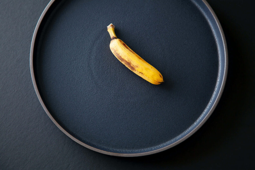 Ripe yellow banana on large dark plate showcasing freshness and vibrant color minimalist background Wallpaper