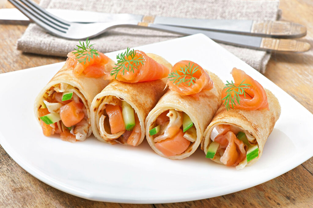 Egg rolls stuffed with fresh salmon and crisp vegetables on white plate with garnish wallpaper background