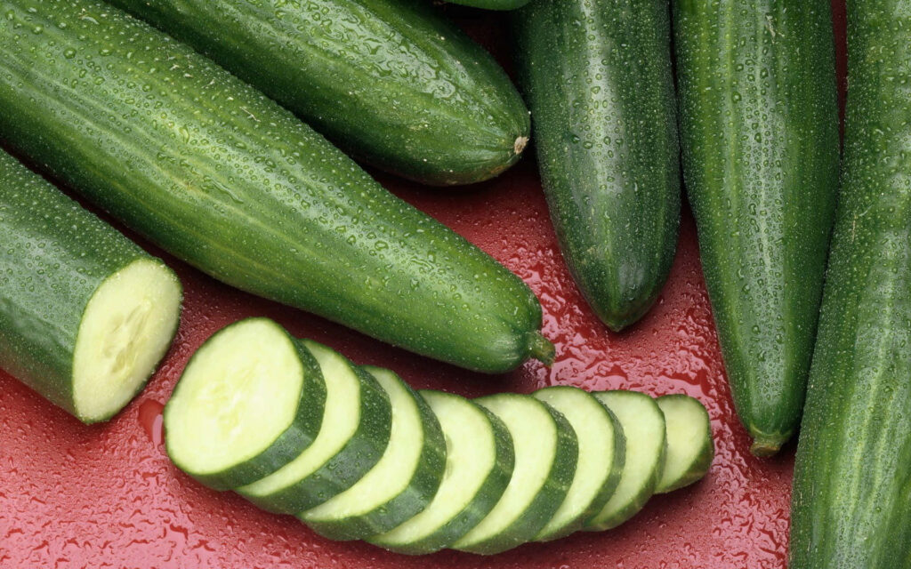 Close-up of fresh crisp cucumber slices on vibrant red background highlighting texture freshness Wallpaper