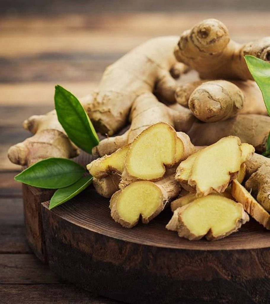 Macro wallpaper of fresh sliced ginger rhizomes on rustic wooden board with green leaves