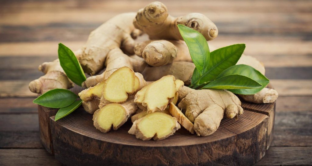 Fresh sliced ginger root with green leaves on rustic wooden platter warm natural light background Wallpaper