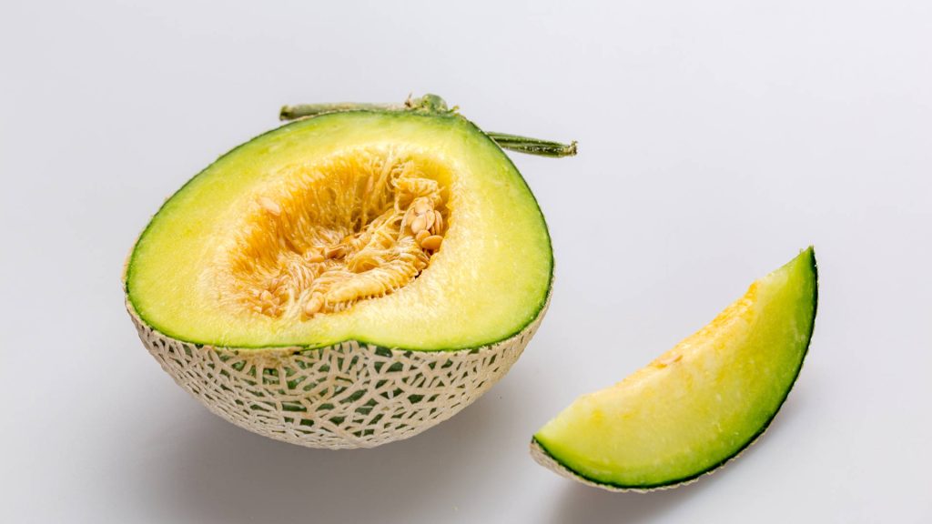 Freshly sliced muskmelon with netted rind and vibrant green flesh on white background Wallpaper