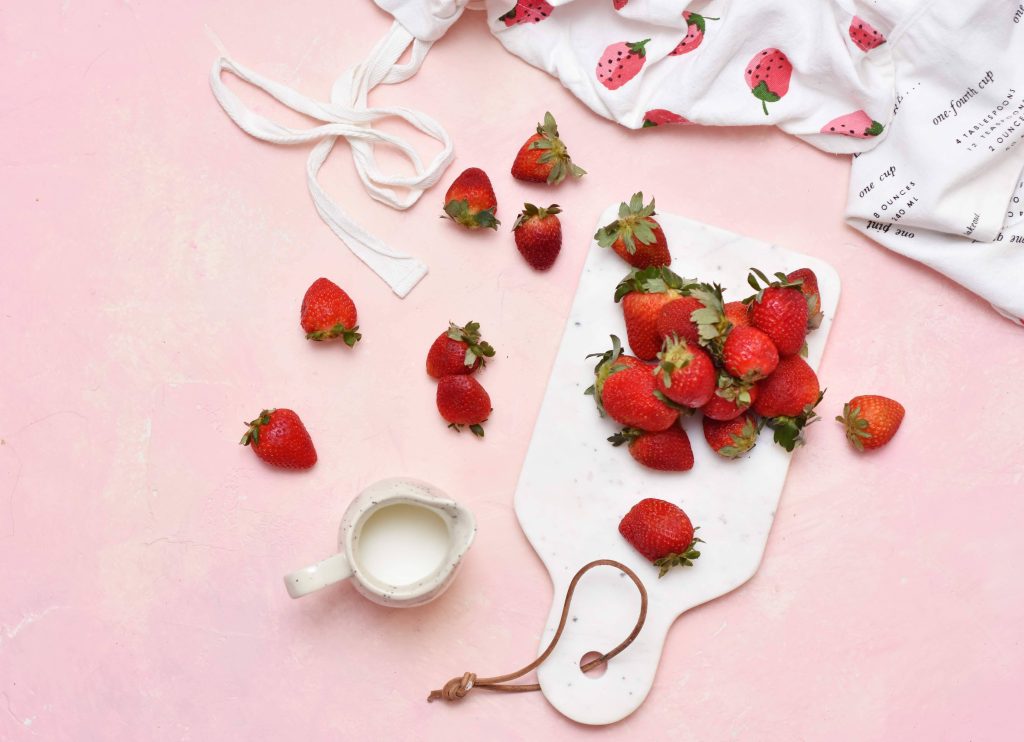 Top-down view of ripe strawberries cream pitcher on marble board with strawberry towel background Wallpaper