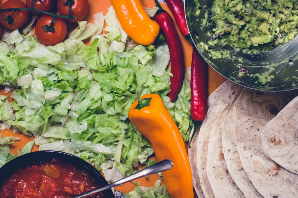 Colorful fresh vegetable burrito ingredients with lettuce tomatoes peppers guacamole and salsa on orange background Wallpaper