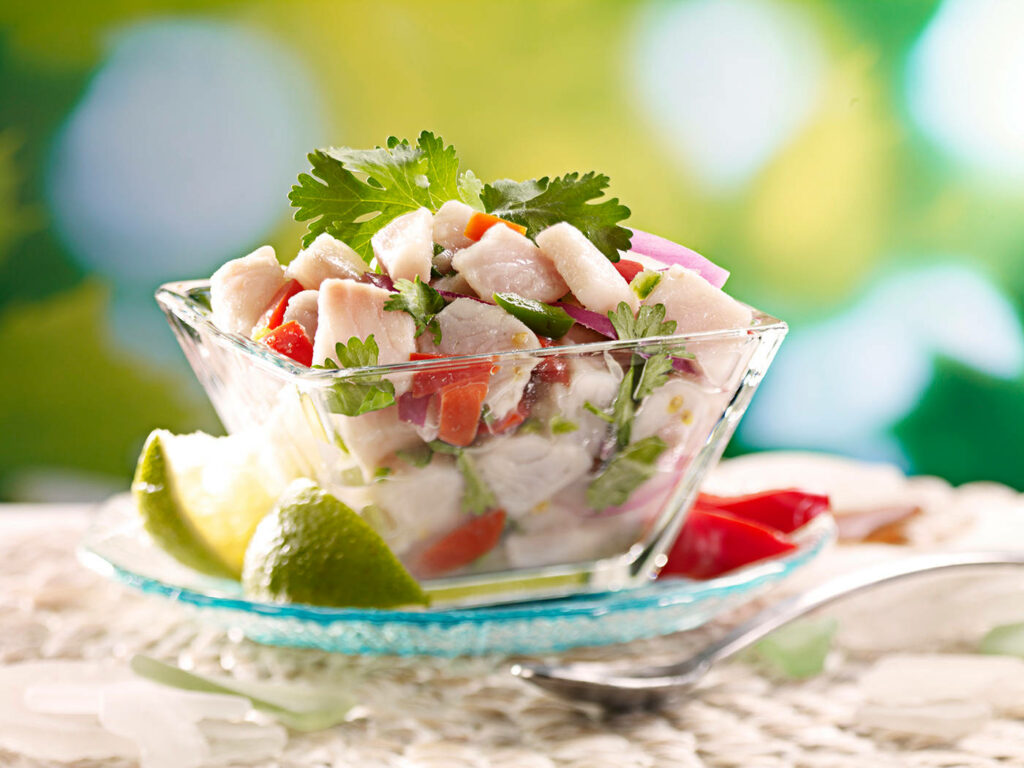 Vibrant ceviche with fresh fish red onions tomatoes cilantro and lime wedges in glass bowl Wallpaper