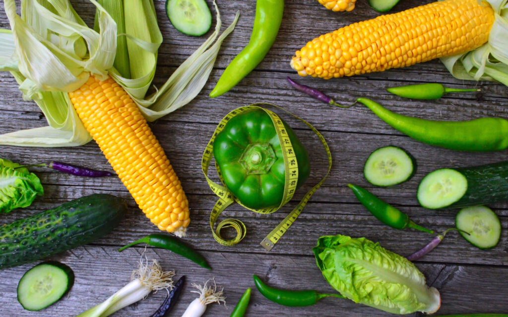 Vibrant corn wallpaper with yellow corn and green vegetables on rustic wooden boards background