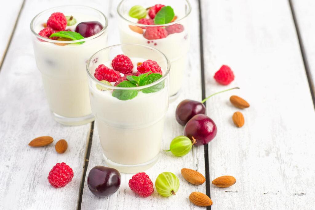 Fresh yogurt with raspberries cherries gooseberries mint and almonds on rustic white wood Wallpaper