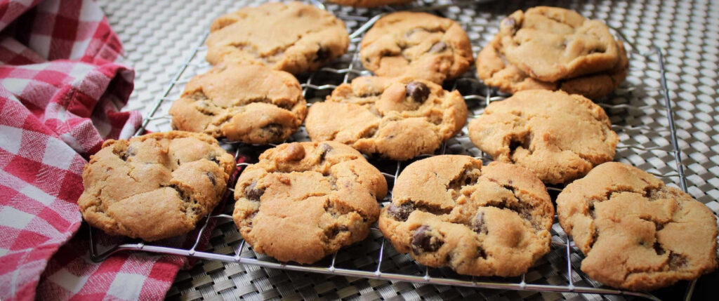 Freshly baked golden chocolate chip cookies cooling on rack with red checkered cloth background Wallpaper