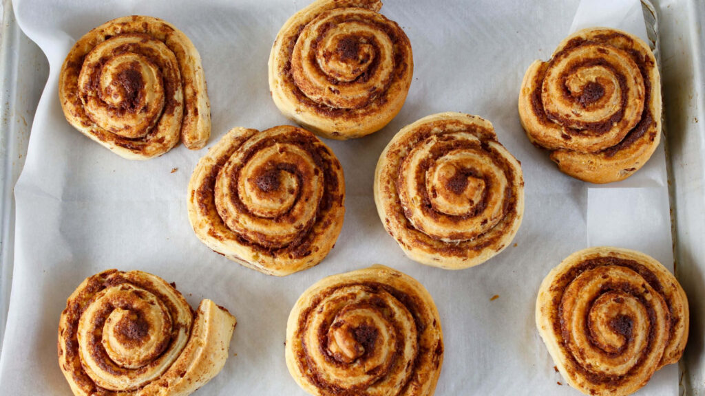 Freshly baked golden cinnamon rolls with visible swirls on parchment paper wallpaper background