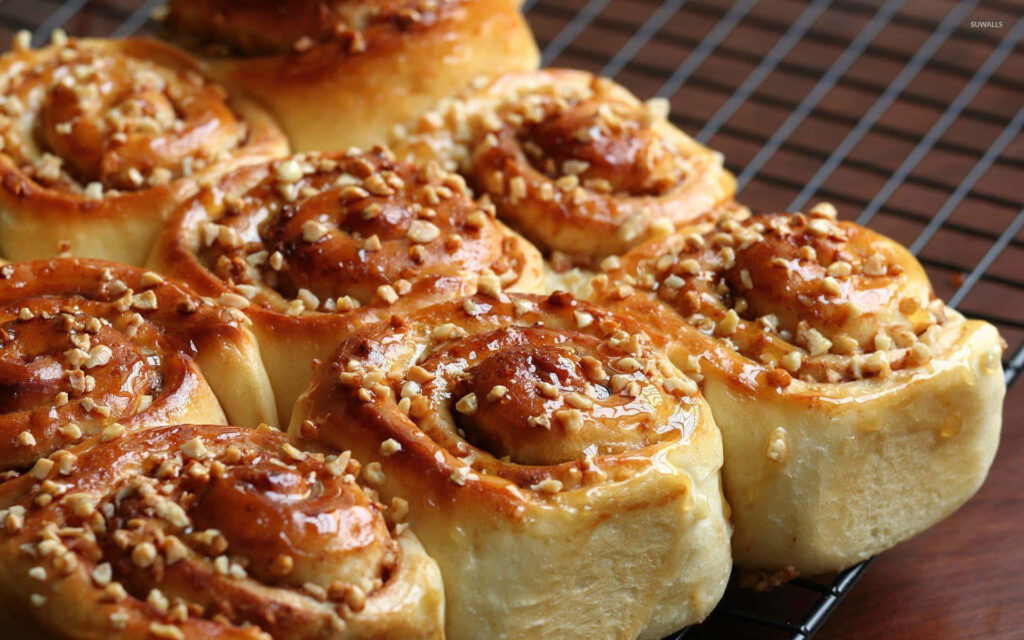 Freshly baked glazed cinnamon rolls with chopped nuts cooling on a rack homemade dessert wallpaper