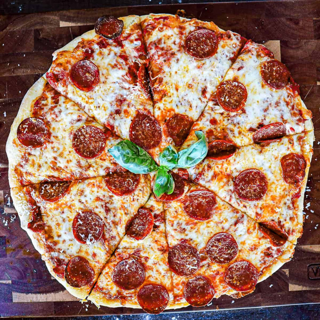 Freshly baked pepperoni pizza with melted cheese and basil on rustic wooden surface wallpaper