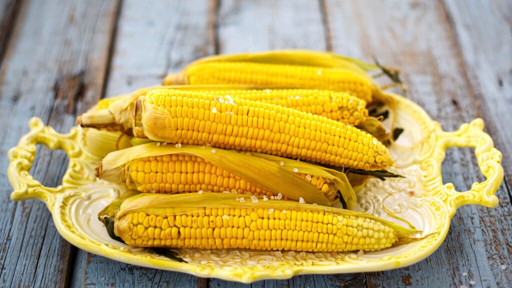 Close up of freshly cooked corn on the cob with coarse salt on yellow platter rustic blue background Wallpaper