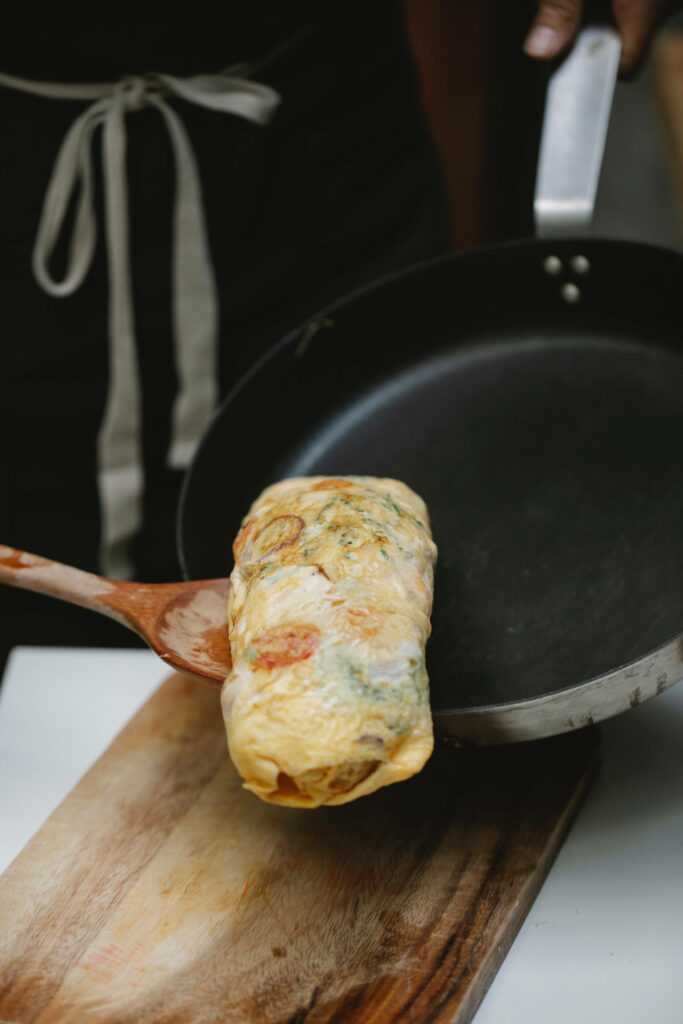 Close-up of freshly cooked egg roll transferred from non-stick pan to wooden board warm tones Wallpaper