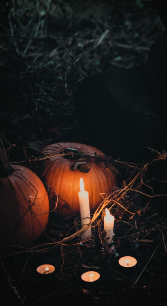 Spooky Illumination: Halloween iPhone Wallpaper featuring Pumpkins and Candlelight creates a Haunting Atmosphere