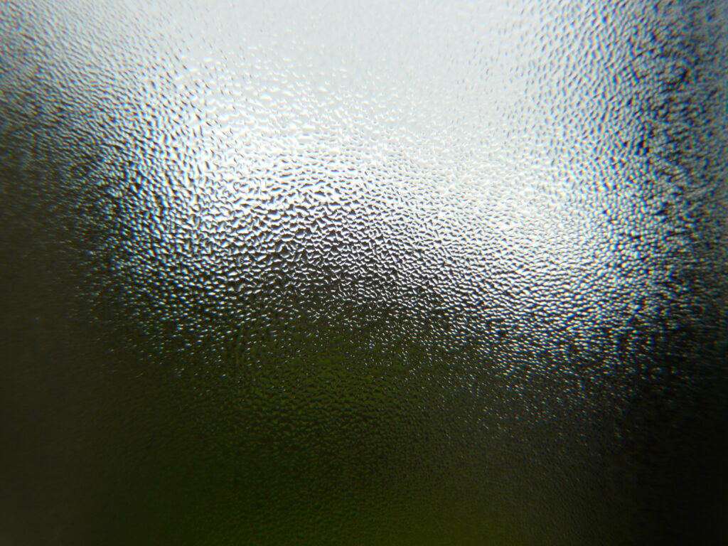 Close-up of textured frosted glass with blurred green and gray tones abstract wallpaper background