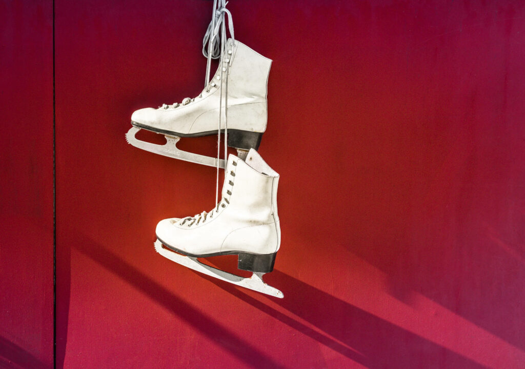 A Charming Ice Skating Tribute: White Skates Gracefully Stand Out Against Vibrant Red Wall Wallpaper