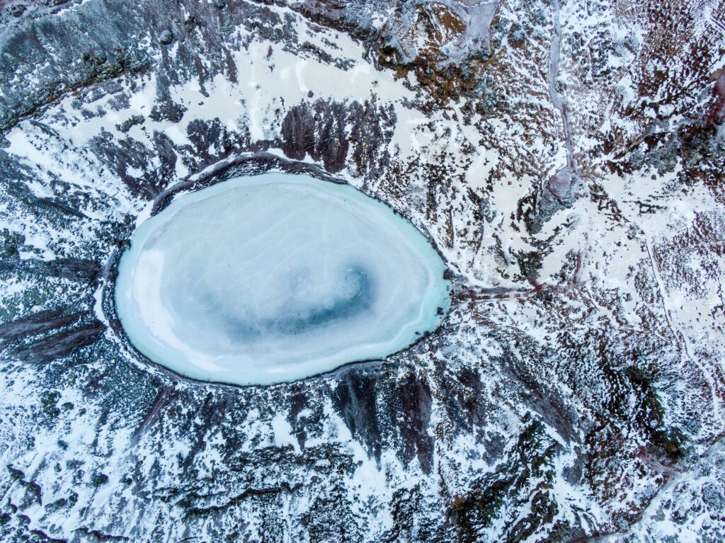 Aerial view of frozen lake with icy textures and snow-covered winter landscape in blue tones Wallpaper
