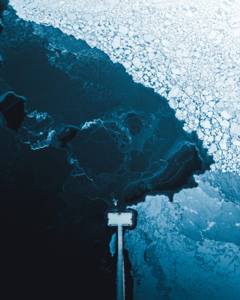 Aerial view of frozen lake with intricate ice patterns and solitary pier over deep blue water winter scene Wallpaper