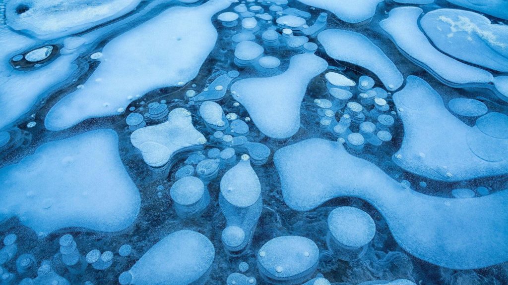 Frozen lake ice with intricate trapped methane bubbles in cool blue winter landscape wallpaper