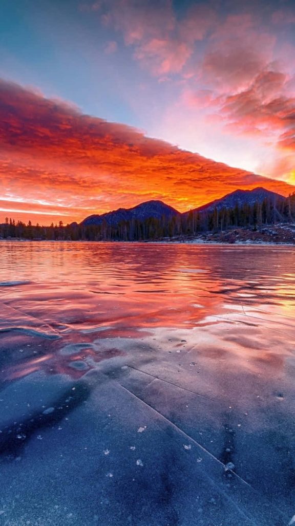 Frozen lake at sunset with cracked ice and vibrant red orange sky winter mountain wallpaper
