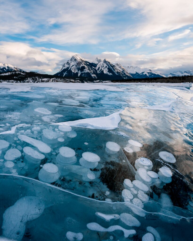 Frozen lake with clear ice and air bubbles against snow-covered mountains in winter landscape Wallpaper