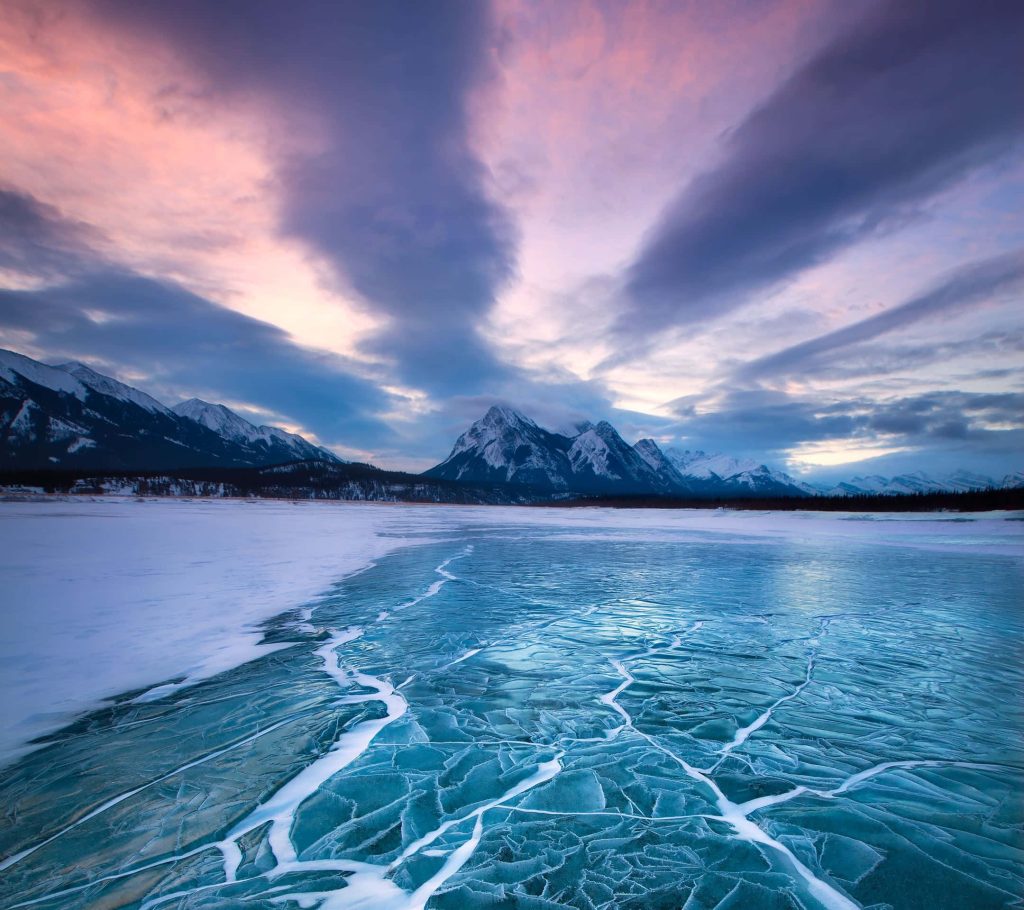 Frozen lake with icy cracks beneath snow-covered mountains and vibrant purple twilight sky wallpaper