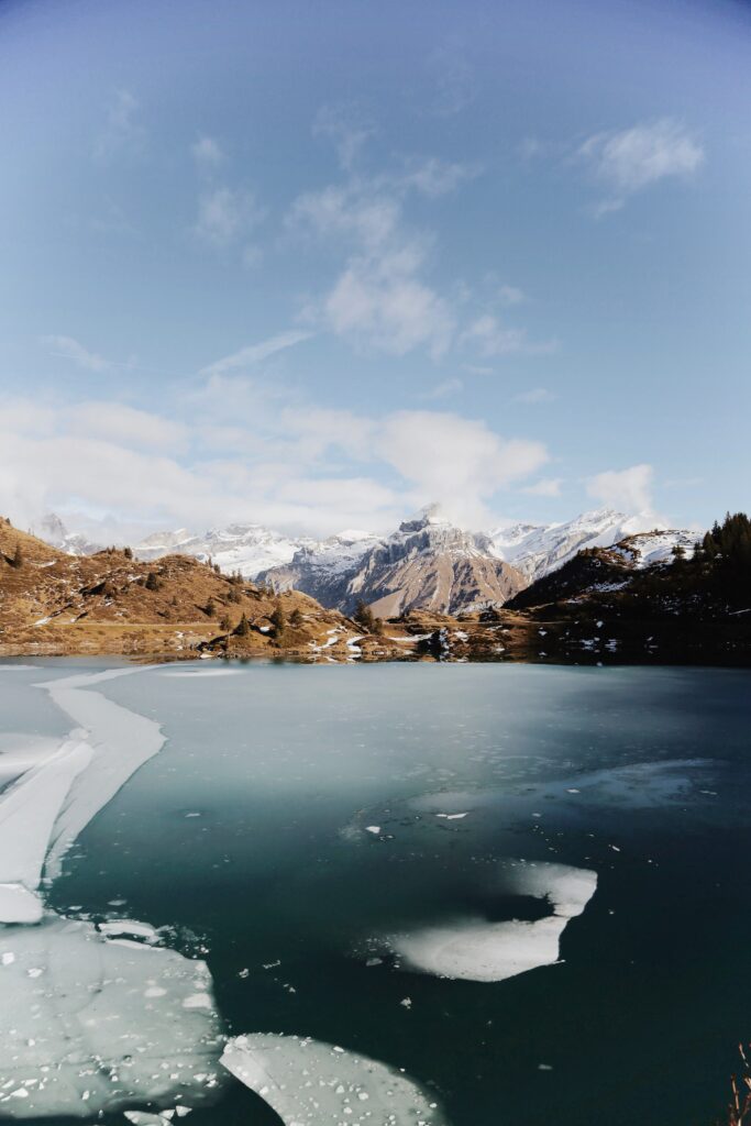 Frozen lake with fractured ice sheets and rugged mountains under clear blue winter sky wallpaper
