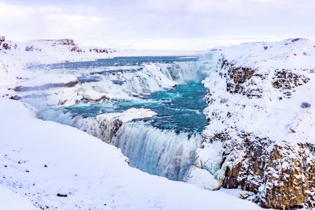 Winter waterfall cascading through icy cliffs with turquoise water and pristine snow background Wallpaper