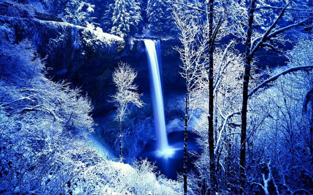 Frozen waterfall cascading over frosty rocks in a snowy forest winter wallpaper background