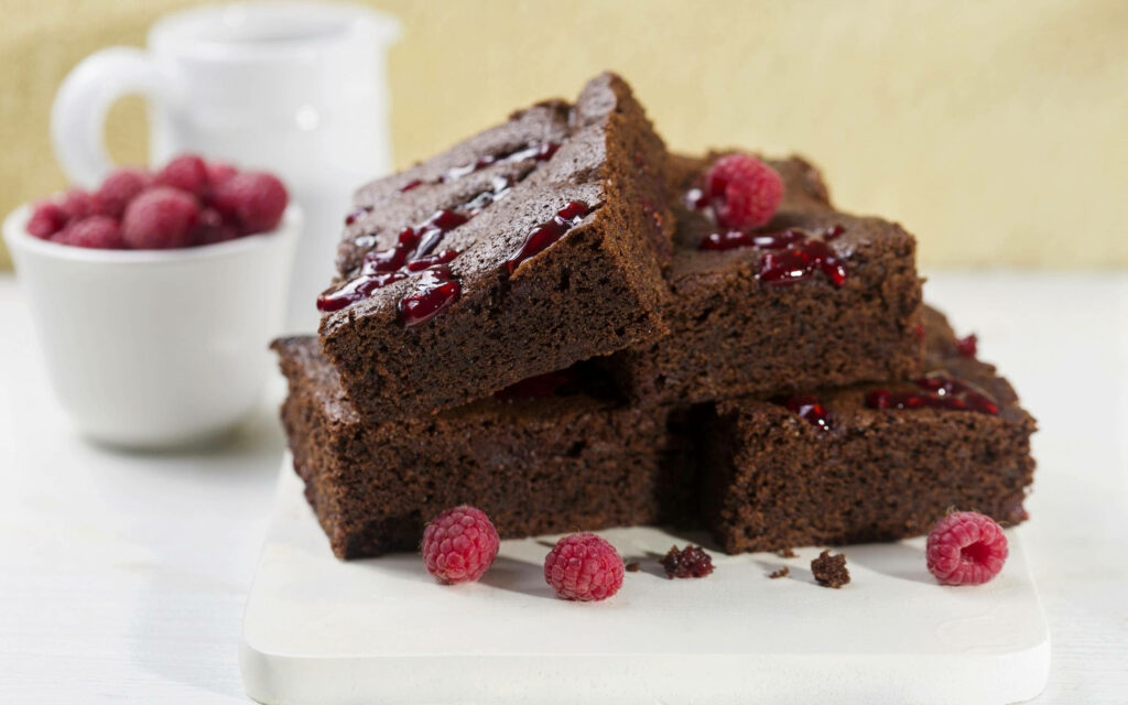Fudgy chocolate brownies stacked with fresh raspberries and glossy raspberry sauce on plate Wallpaper